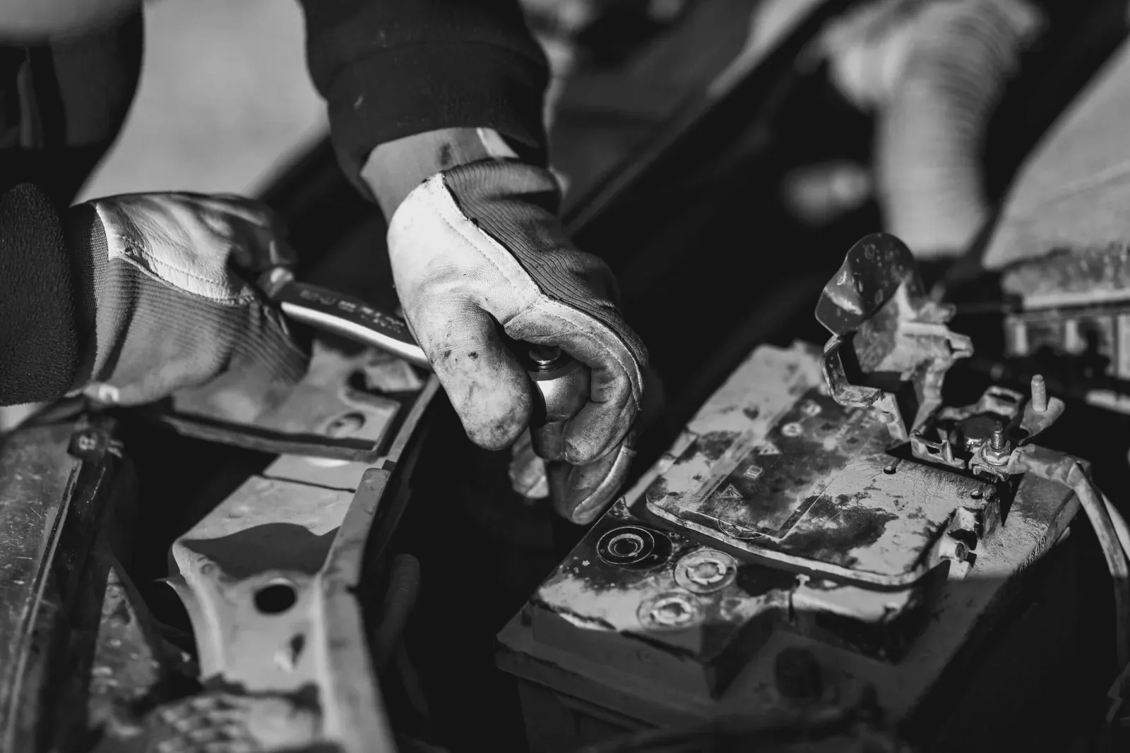 Monteur met werkhandschoenen maakt de pool van een oude accu los om hem te vervangen